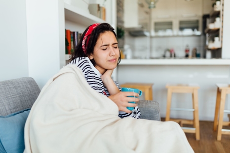woman with sore throat on couch with cup of tea